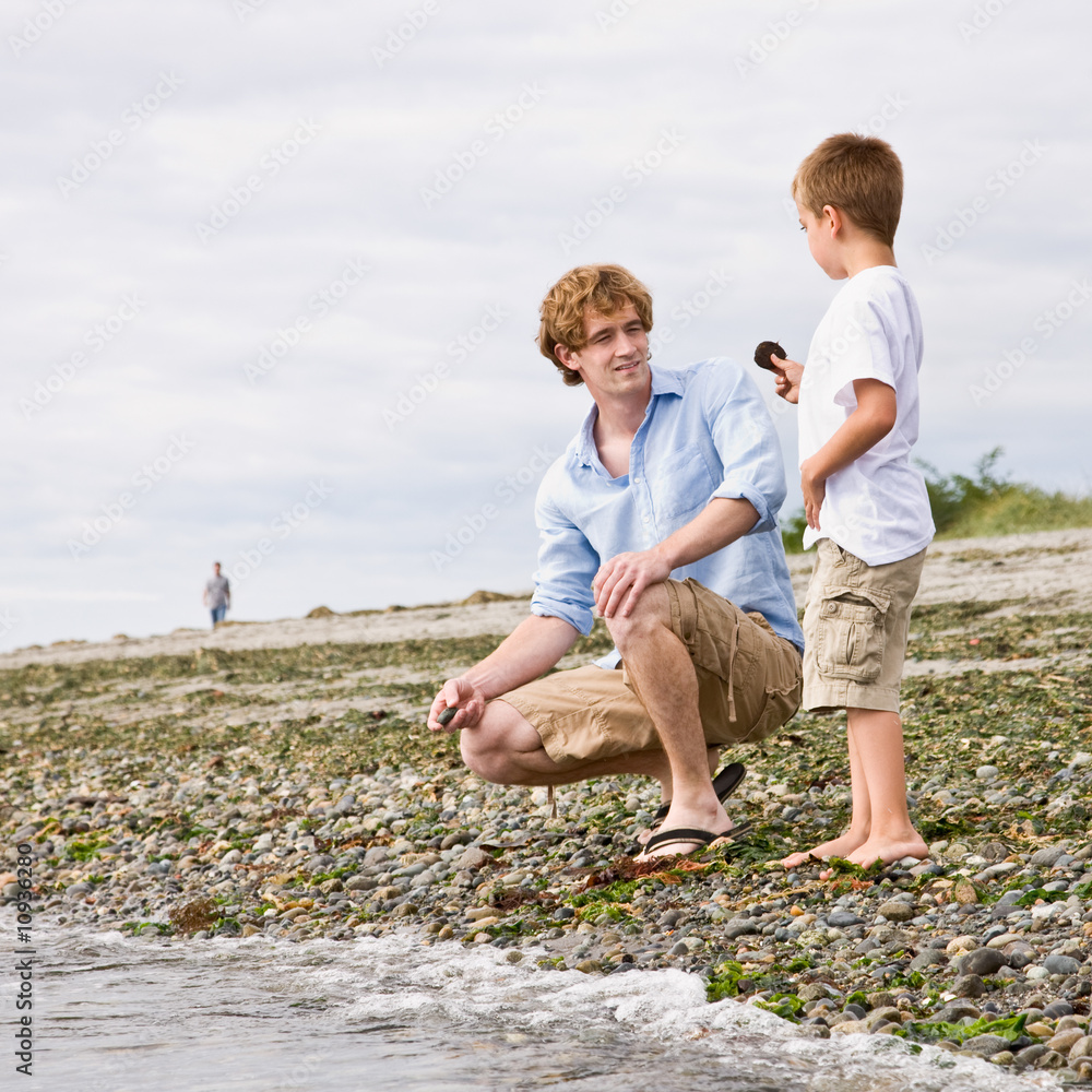 Fototapeta premium Father and son gathering rocks at beach