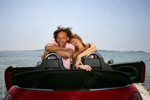Jeune couple dans voiture décapotable face à la mer