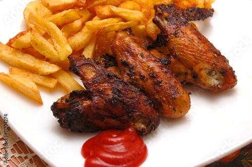 Grilled chicken wings on a white plate with chips.