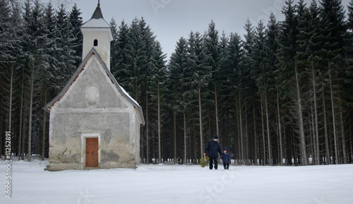 Vater und kleiner Sohn neben Waldkapelle im Winter photo