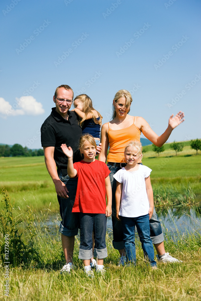 Familie auf der Wiese vor dem Teich winkt Familie auf der Wiese vor dem Teich winkt