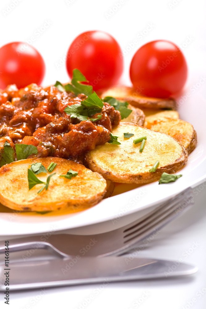 roasted potatoes with meat tomato sauce, a fork and a knife roasted potatoes with meat tomato sauce, a fork and a knife