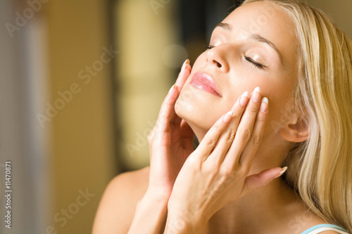 Portrait of young happy woman applying facial cream photo