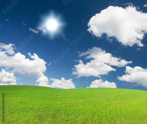 Green hill under blue cloudy sky whit sun © Alexander Ozerov
