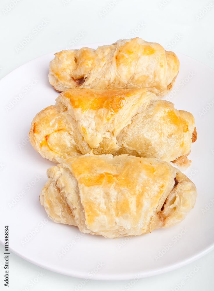 three sausage rolls on a white plate on a white background