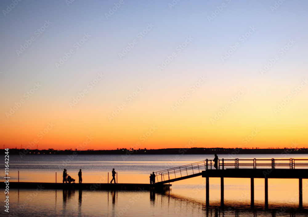 A view of silhouetted people walking on a pier