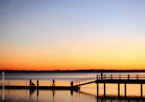 A view of silhouetted people walking on a pier © Jakub Krechowicz