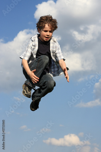 Kid running, jumping on green meadow against blue sky