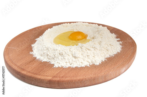 Flour and eggs on a wooden round board.