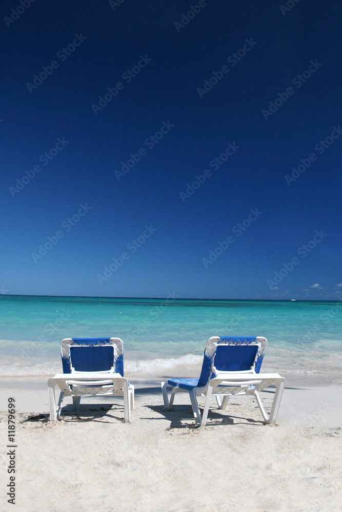 Two Lounge Chairs on White Sand Beach and Ocean Background Two Lounge Chairs on White Sand Beach and Ocean Background