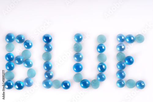 The word BLUE created and written by blue and turquoise glass stones on white background.