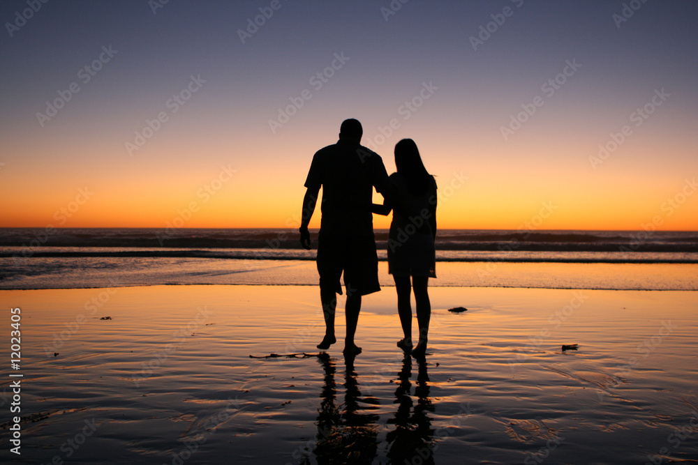 A couple walks on the beach at sunset