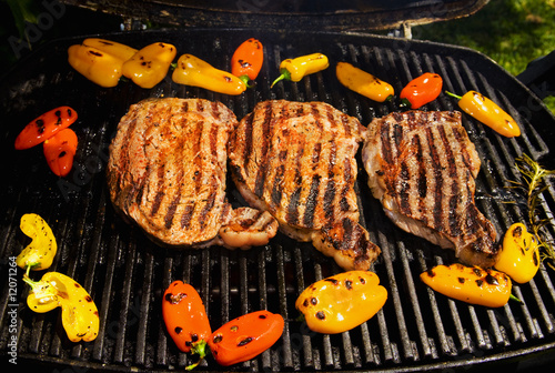 ribeye steaks cook on the bar-b-que grill with bell peppers