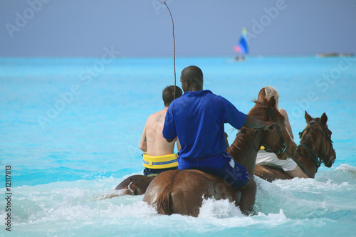 People horseback riding in tropical island beach ocean