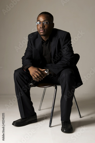 black male sitting on a chair with hand clasped