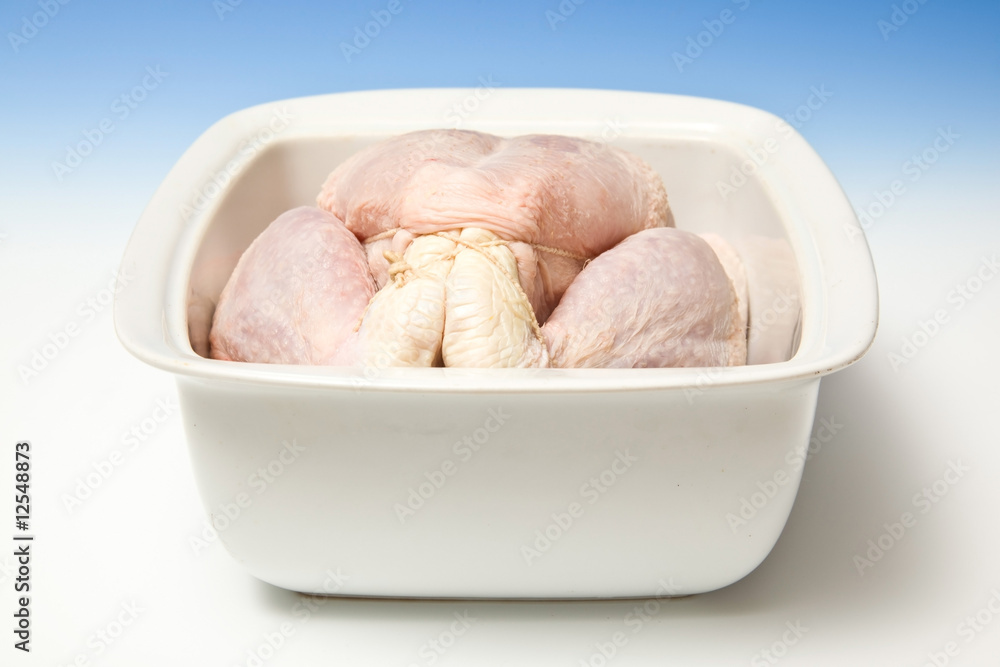 Whole raw chicken in a roasting dish on a blue studio background Whole raw chicken in a roasting dish on a blue studio background