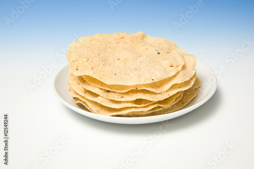 Plate of fresh pappadums on a blue studio background.