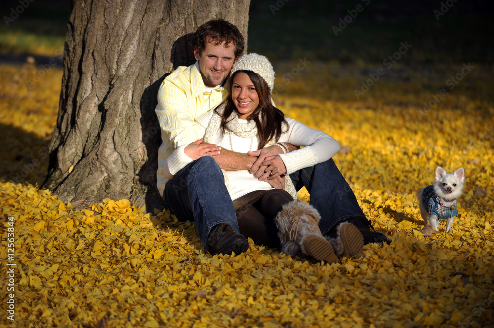 Smiling attractive young couple sitting in leaves with dog.