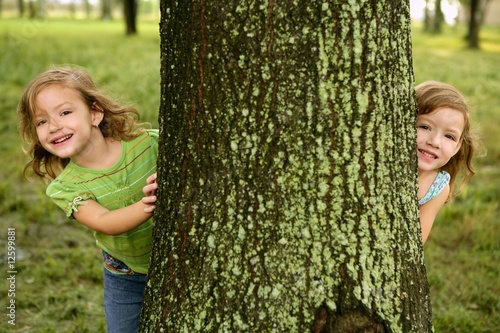 Two twin little girls playing in tree trunk photo