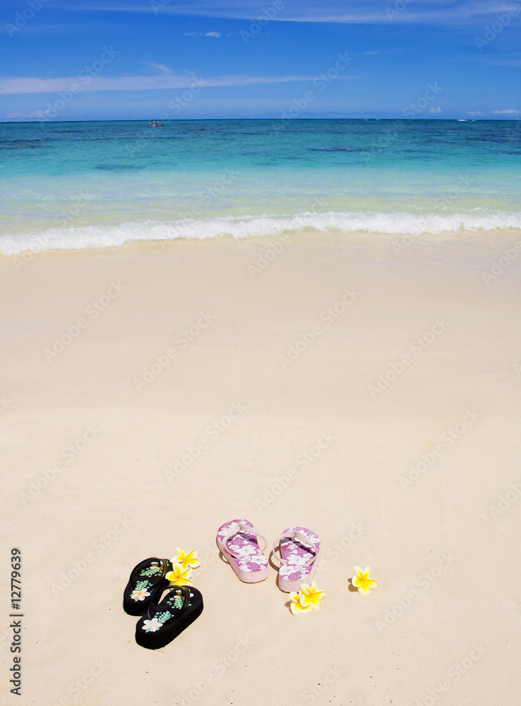 pairs of sandals and a plumeria blossom on a Hawaii beach