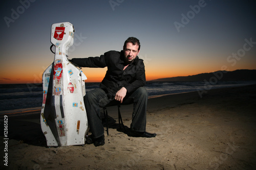 Musician with travel cello or guitar case on beach at sunset photo