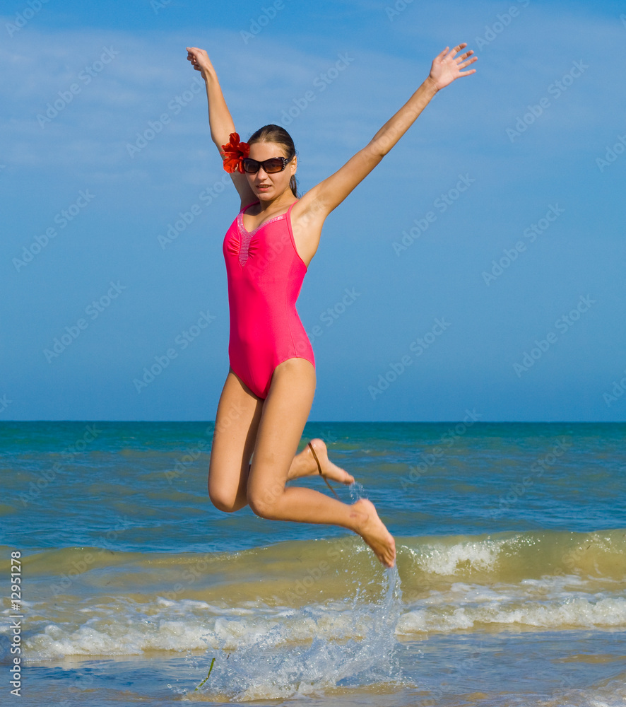 Girl in pink swimsuit jumping on a beach