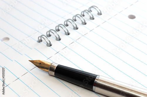 A gold-nibbed pen on a spiral-bound notepad