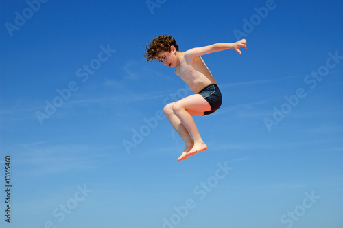 Fototapeta Naklejka Na Ścianę i Meble -  Boy jumping against blue sky