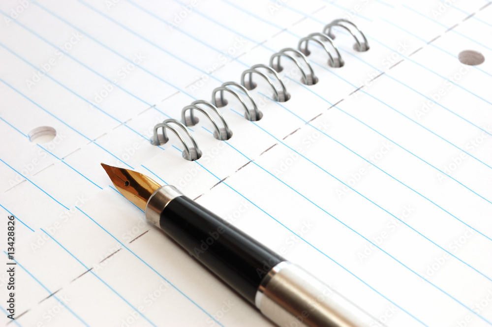 A gold pen on a spiral-bound notepad A gold pen on a spiral-bound notepad
