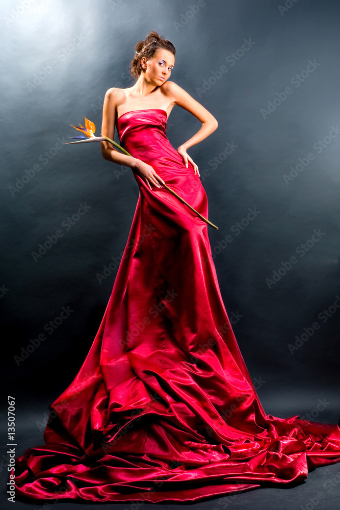 Fototapeta premium Beautiful girl in a long red dress holds exotic flower in a hand
