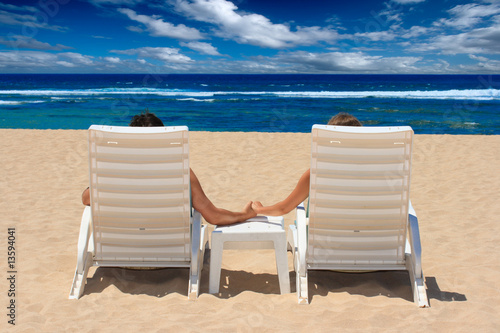 Couple in beach chairs holding hands near ocean