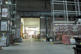 Industrial warehouse interior with high shelves stocked with pallets, a clear pathway leading to an open gate, and natural light entering from outside.