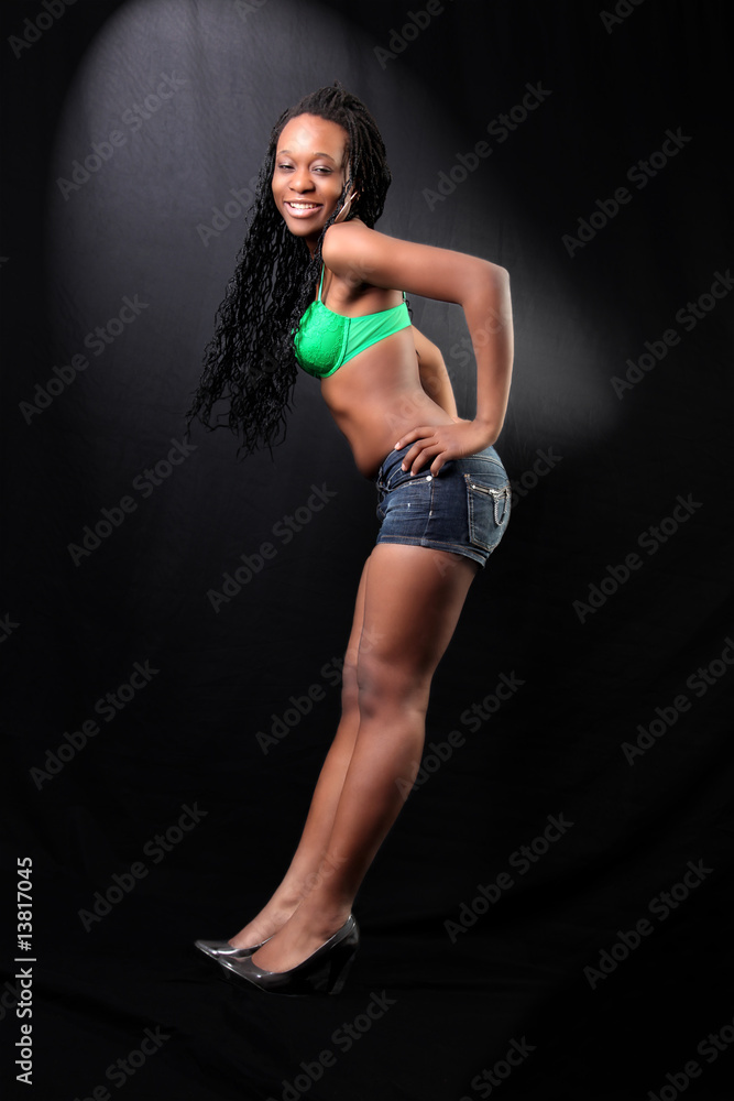 young afro-american woman in bra and shorts against black backgr