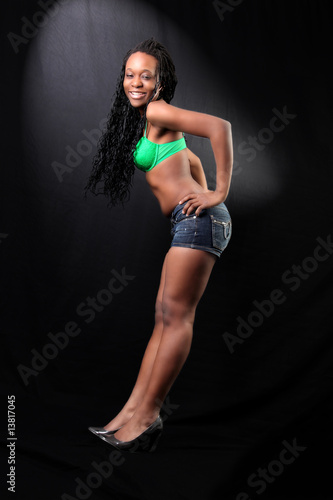 young afro-american woman in bra and shorts against black backgr