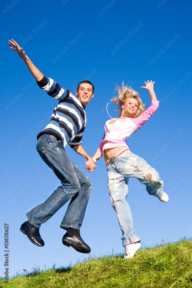 Happy young couple jumping in sky above a green meadow Happy young couple jumping in sky above a green meadow