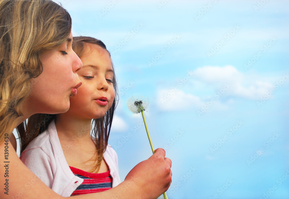 Sisters blowing dandelion on a meadow and have fun Sisters blowing dandelion on a meadow and have fun