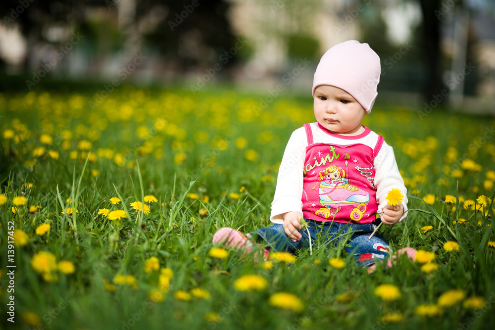 baby sits on a green grass in dandelions