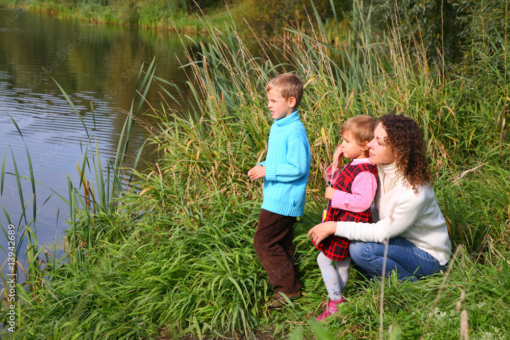 Fototapeta premium Mother with children sits on bank of pond