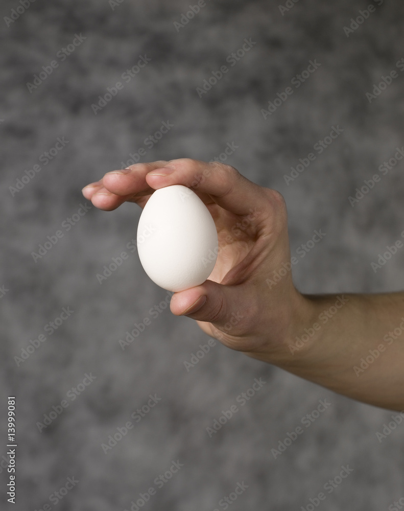 Hand holding an egg towards grey background Hand holding an egg towards grey background