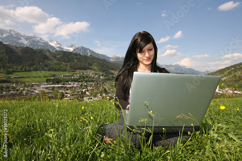 Mädchen mit Laptop in Wiese / Hintergrund Schladming