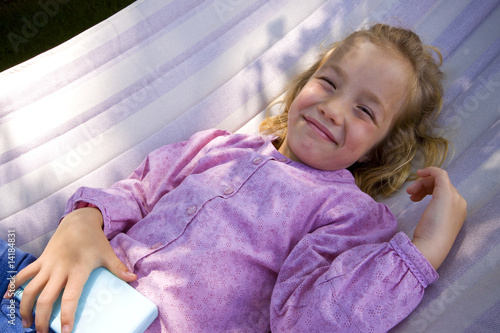 little girl plays with a portable game console in a hammock
