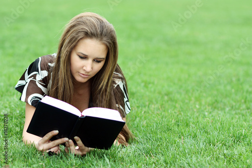 Young beautiful woman lays on green field and reads book