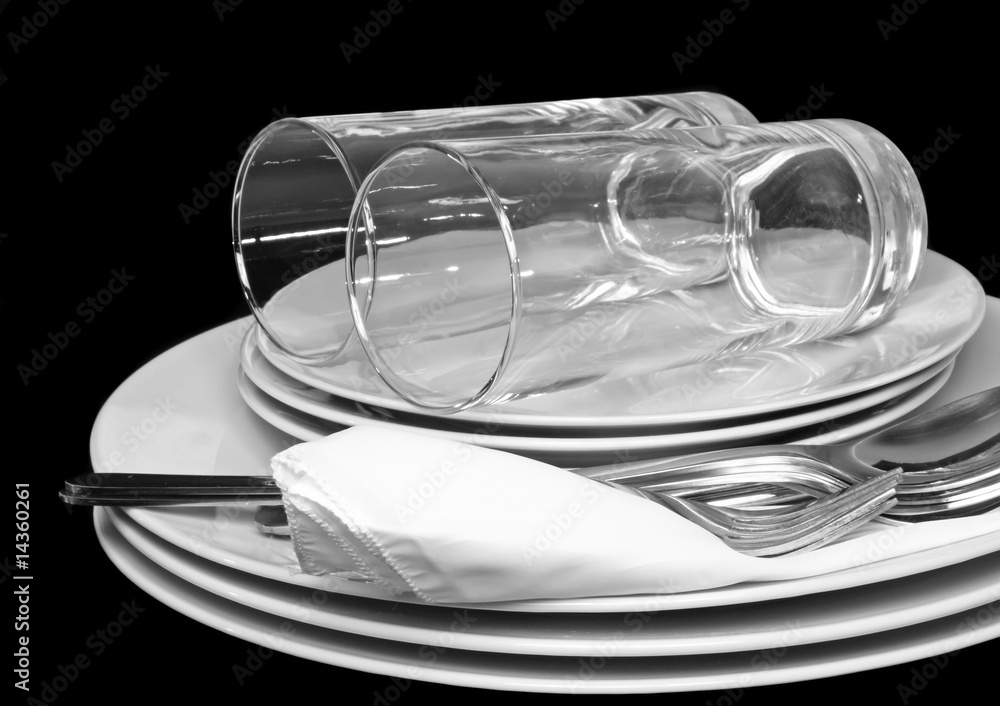 Pile of white plates, glasses with forks, spoons,silk napkin.