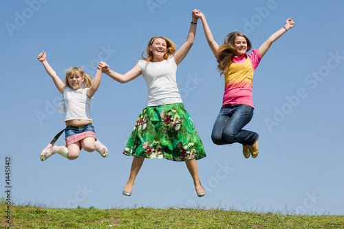 Happy Mother and two daughter jumping on green meadow