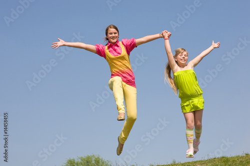 Two girls jumping on green meadow