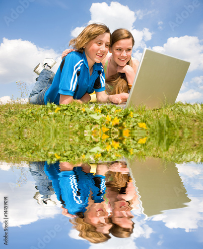 Two Smiling teenagers with laptop resting on meadow