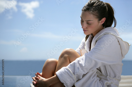 Jeune femme en peignoir assise au bord d'une piscine