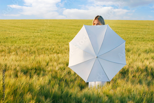 young beautiful girl behind white umbrella in green field