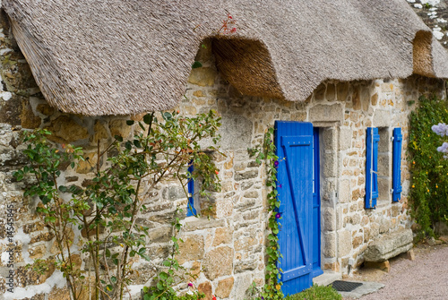 Traditional stone house with blue shutters and thatched roof in