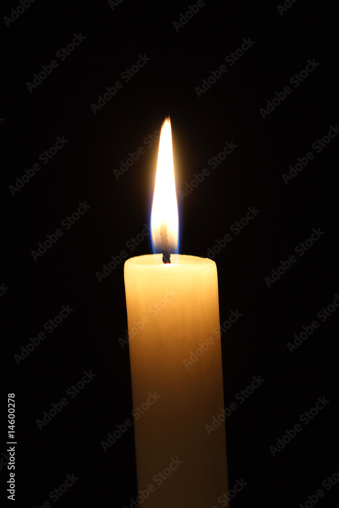 A burning candle against a black background. A burning candle against a black background.